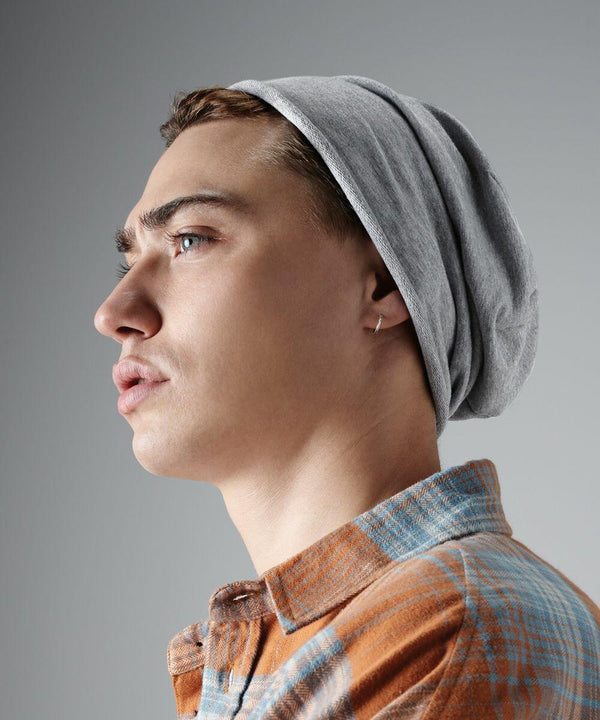 A young person with light skin and short brown hair wears a gray Beechfield BC361 beanie and an orange and blue plaid shirt. They have a small hoop earring and are looking to the left against a plain gray background.