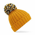 A Beechfield BC390 mustard-yellow ribbed knit beanie featuring a folded brim and topped with a large pom-pom in black, white, and mustard colors is positioned at an angle against a white background.