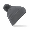 The Beechfield BC426 is a gray knitted beanie featuring a large pom-pom on top, presented against a plain white background. The beanie is angled to one side, highlighting its soft texture and folded brim.