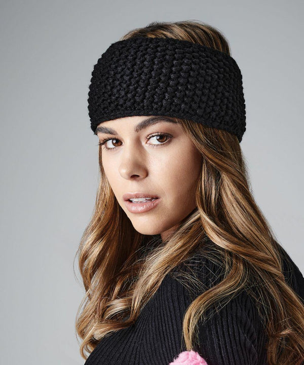 A woman with wavy, light brown hair wears a Beechfield BC434 headband and a black sweater. She looks directly at the camera with a neutral expression. The background is plain grey.