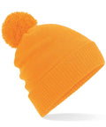 A Beechfield BC439 knitted beanie in orange, featuring a large pom-pom on top. The hat is showcased against a white background, angled slightly to the right.