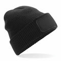 A Beechfield BC440 black knit beanie featuring a blank patch on the front, set against a white background.