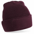 The BC445 by Beechfield is a maroon knit beanie featuring a folded brim and a rectangular patch on the front, with a ribbed texture that provides a cozy and warm look.