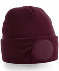Beechfield's BC446 is a maroon beanie hat featuring a ribbed texture and a folded brim, accented by a circular patch on the front.