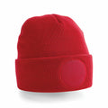 Introducing the Beechfield BC446, a vibrant red knitted beanie featuring a circular patch prominently displayed on the front of its folded brim. Designed with a snug fit and textured look, it stands out against a simple white background.