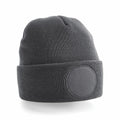 The Beechfield BC446 is a gray knit beanie featuring a folded brim and a circular patch on the front. It boasts a ribbed texture, giving it a soft and warm appearance against the plain white background.