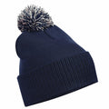 The Beechfield BC450 is a navy blue knit beanie featuring a large pom-pom on top. It showcases a ribbed texture and a folded cuff at the bottom, with the pom-pom made from a playful mix of white and blue yarn.