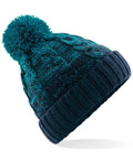 The Beechfield BC459 is a knitted beanie adorned with a large pom-pom on top. It showcases a cable knit pattern in shades of teal and dark blue for a cozy and warm look. The brim is ribbed to ensure a snug fit.