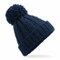A Beechfield BC480 beanie in navy blue, showcasing a pom-pom on top, along with a ribbed brim and cable knit pattern, displayed against a white backdrop.