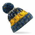 The Beechfield BC486 is a knitted winter hat with a large pom-pom on top, showcasing a color pattern of navy blue, yellow, and white. Its brim is a solid gray-blue color, and the hat is set against a plain white background.