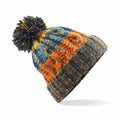 The Beechfield BC486 is a vibrant knitted beanie adorned with a pom-pom on top, showcasing an array of patterns in blue, orange, and yellow against a white background.