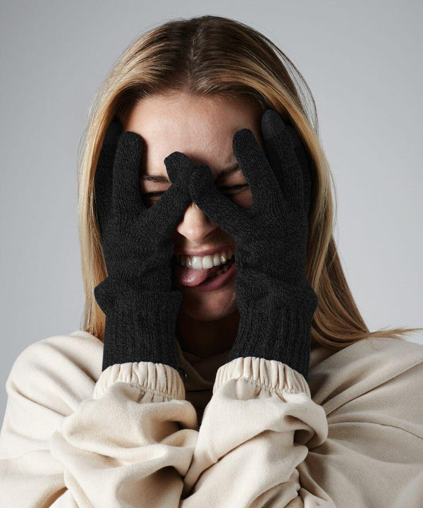 A person with long hair is playfully covering their face with **Beechfield BC490**, forming a mask around their eyes with their fingers. They are smiling widely and wearing a beige or off-white top against a plain light gray background.