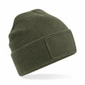 The Beechfield BC540 is a green knit beanie featuring a ribbed texture, a folded brim, and a blank rectangular patch on the front. It is showcased against a plain white background.