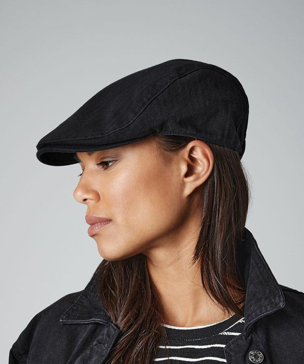 A person with long straight hair is wearing a black BC626 by Beechfield, a matching black jacket, and a black and white striped shirt. The person is facing the left side, displaying their profile against a plain gray background.