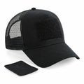 A Beechfield BC641 black trucker cap featuring a mesh back and a square Velcro patch on the front, displayed with an additional Velcro patch.