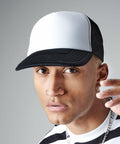 A person wearing a black and white Beechfield BC645 trucker hat and a nose ring gazes directly at the camera. The person has short, light-colored hair and is dressed in a black and white striped shirt. A hand is partially visible near the face, as though mid-motion.