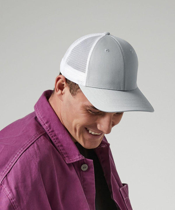 A person wearing a light gray Beechfield BC646 baseball cap with a white mesh back, and a purple jacket. The person is smiling and looking downwards against a neutral background.