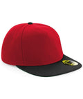 Beechfield's BC660 snapback cap, featuring a red front panel and top button with a black flat brim, is displayed at an angle. A small round sticker on the brim provides details about the cap.