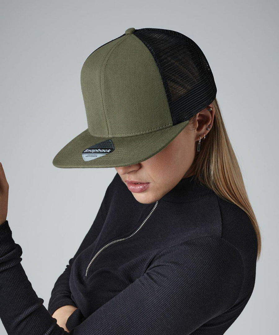 A person wearing a dark olive green Beechfield BC664 trucker cap with a black mesh back, styled with silver hoop earrings and a black zippered top. The individual's head is slightly tilted down, obscuring their face partially from view. The background is plain grey.