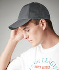 A person wearing a gray Beechfield BC75R baseball cap and a white T-shirt with the words "Team League World Champs" printed on it. The person is looking down and touching the side of the cap with one hand. The background is plain and neutral.