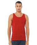 A man with short hair is standing and facing the camera. He is wearing a sleeveless, red Bella Canvas BE104 tank top and dark blue jeans. The background is plain white.