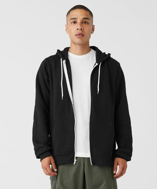 A person stands facing the camera wearing a Bella Canvas BE106 black zip-up hoodie with white drawstrings and a white T-shirt underneath. They also wear olive green pants. The background is plain and white.