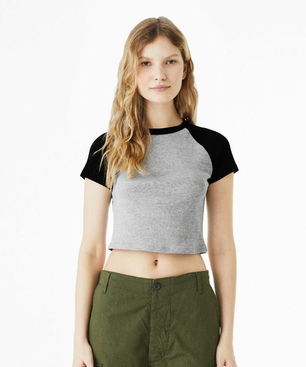 A person stands against a white background, wearing a Bella Canvas BE143 short-sleeve crop top with black raglan sleeves and green pants.