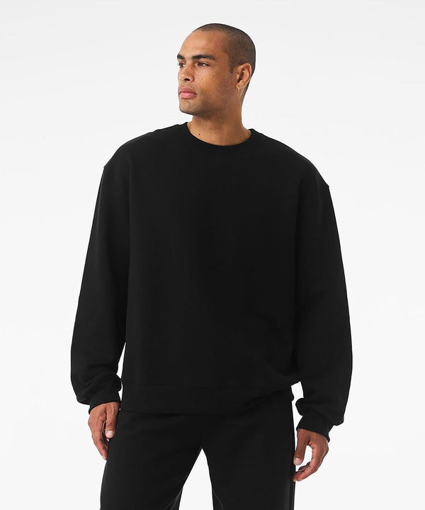 A person wears a Bella Canvas Unisex crew neck heavy sweatshirt paired with black trousers, standing against a white background and gazing to the side with a neutral expression.