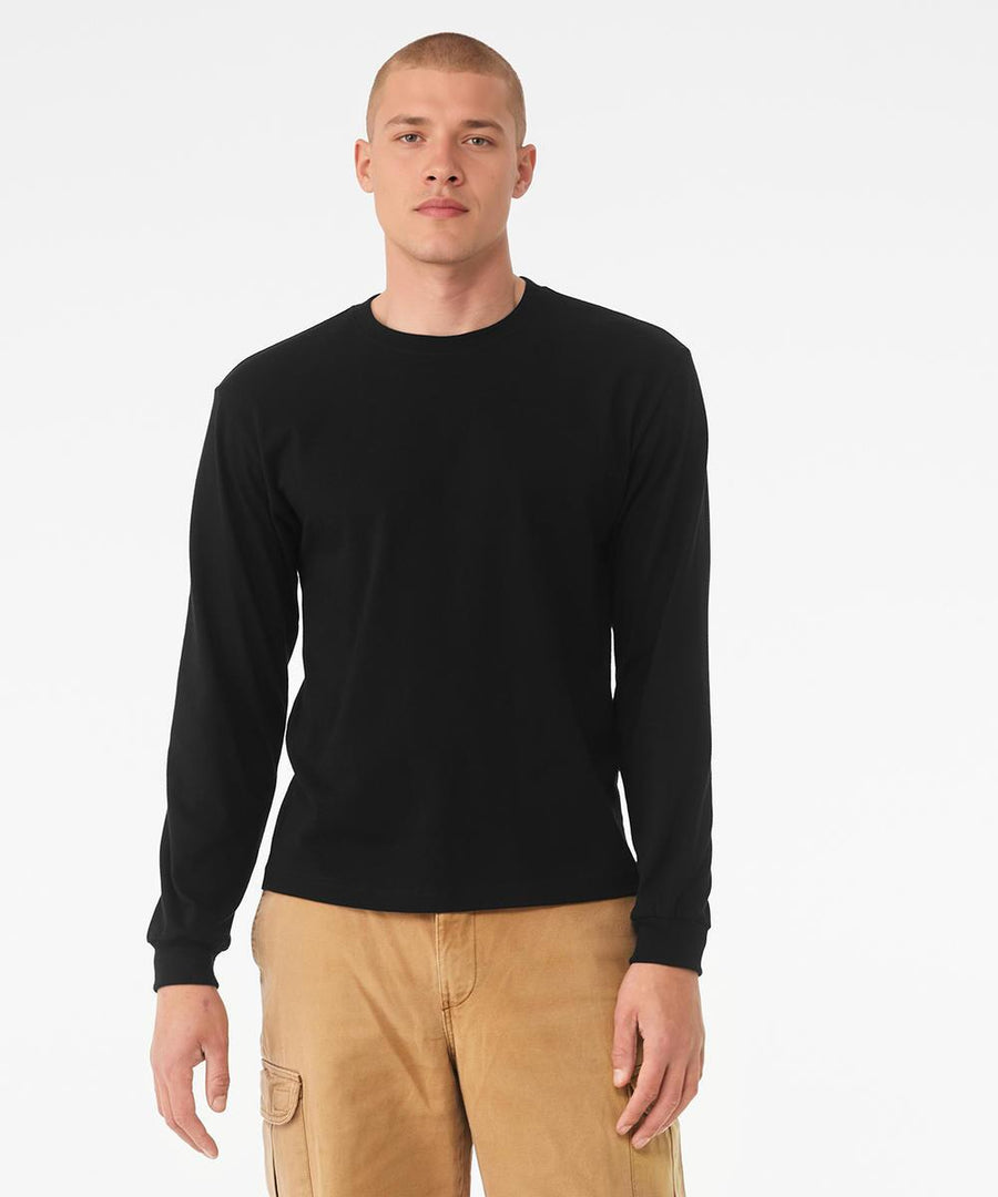 A person with short hair is wearing the Bella Canvas Unisex heavy boxy long-sleeve tee in black and light brown cargo trousers, standing against a plain white background.