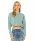 A person with long blond hair is wearing a light green cropped sweatshirt and high-waisted blue jeans. They are standing against a plain white background, looking directly at the camera with a neutral expression. The sweatshirt is the BE221 by Bella Canvas.