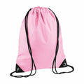 The BG010 by Bagbase is displayed as a pink drawstring backpack featuring black straps and corner reinforcements. The drawstrings extend from the top and pass through metal eyelets at the bottom corners.