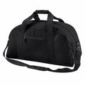 BG022 by Bagbase is a black duffel bag featuring a front zipper pocket, two short handles, and an adjustable shoulder strap, all showcased against a white background.
