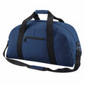 The Bagbase BG022 is a dark blue duffel bag featuring black straps and a front zipper pocket.