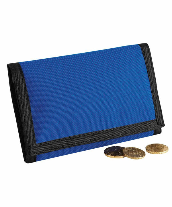 A Bagbase BG040 blue fabric wallet with black edges is placed on a surface next to three coins.