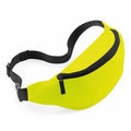 Introducing the Bagbase BG042: a vibrant yellow fanny pack featuring a sleek black adjustable strap and a stylish black zipper. The bag is artfully showcased at an angle, highlighting its elegant curved shape and convenient front zipper closure.
