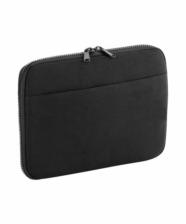 A black zippered sleeve designed to hold a tablet or small laptop. The BG065 by Bagbase has a streamlined design with a zip closure on the top edge and an extra front pocket for additional storage. The material appears to be neoprene or a similar fabric.