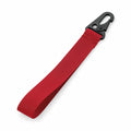 A Bagbase BG100 red fabric strap with a black plastic hook clip at one end is placed diagonally on a white background.