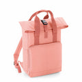 The Bagbase BG118 is a coral-colored backpack featuring a top flap with a buckle closure and a front zip pocket. It is equipped with two shoulder straps and two carrying handles.