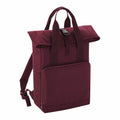 A maroon BG118 backpack from Bagbase features a roll-top design, front zipper pocket, and adjustable shoulder straps. It includes a top handle and is secured with a black buckle.
