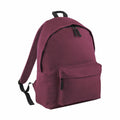 The Bagbase BG125 backpack features a maroon color with black straps and zippers. It includes a large main compartment and a front zippered pocket. The backpack is displayed standing upright against a white background.