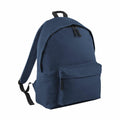 The BG125 by Bagbase is a simple navy blue backpack featuring a front zipper pocket and adjustable shoulder straps. The bag is pictured standing upright on a white background.