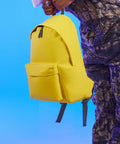 Person holding a bright yellow Bagbase BG125 against a blue background. Only their hand and part of their camo-patterned clothes are visible.