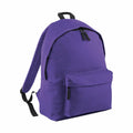Presenting the Bagbase BG125: This purple backpack features black zippers and adjustable shoulder straps, showcased against a pristine white backdrop. The design includes a spacious main compartment and an additional front pocket for extra storage.