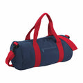 The Bagbase BG140 is a cylindrical navy blue duffel bag featuring bright red handles and straps. It includes a zippered pocket on the side and comes with a detachable shoulder strap. The design is simple and sporty.