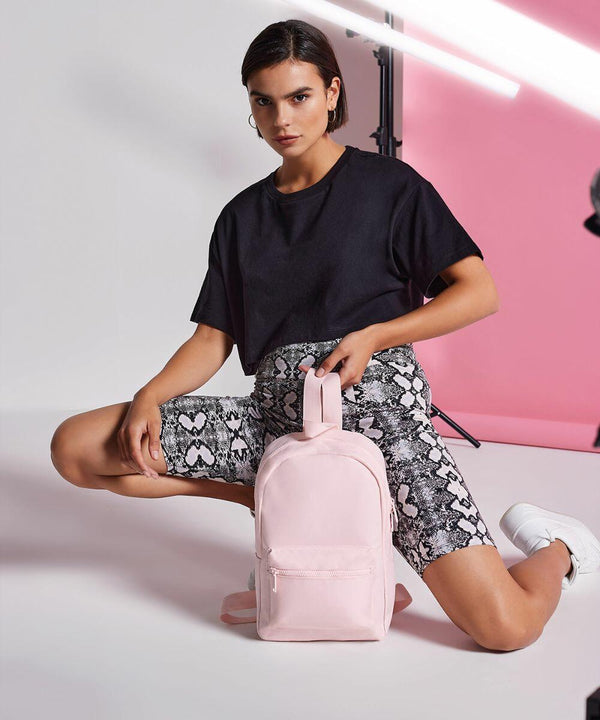 A person dressed in a black t-shirt and snake-print shorts kneels on one knee while holding a Bagbase BG153. The background features pink and white lighting setups.