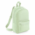 A Bagbase BG153 backpack in light green is displayed with its front zippered pocket and adjustable shoulder straps. The bag is standing upright, highlighting its simple design and top handle.