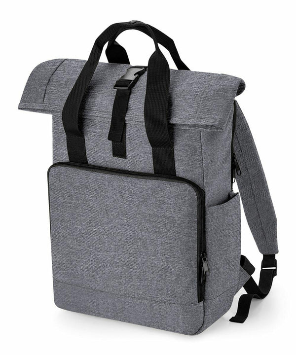 A sleek, gray Bagbase BG18L featuring a top flap secured with a black buckle, padded shoulder straps, and a front zippered compartment. The bag has a minimalist design with a textured fabric appearance and a small side zipper pocket.