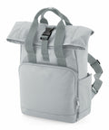 A light grey Bagbase BG18S with a top flap secured by a black buckle. It features two straps for carrying, a front zippered pocket, and an additional side pocket. The fabric appears durable and the design is modern and functional.