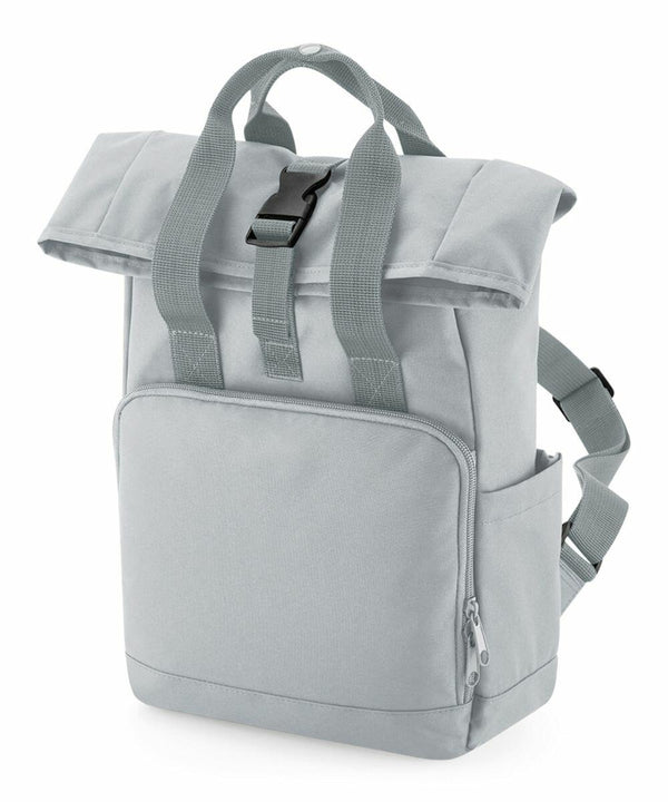 A light grey Bagbase BG18S with a top flap secured by a black buckle. It features two straps for carrying, a front zippered pocket, and an additional side pocket. The fabric appears durable and the design is modern and functional.