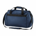 Standing upright against a white background, the Bagbase BG200 features a blue body with black straps and zippers, includes a main compartment, a front zipper pocket, and comes with an adjustable shoulder strap.